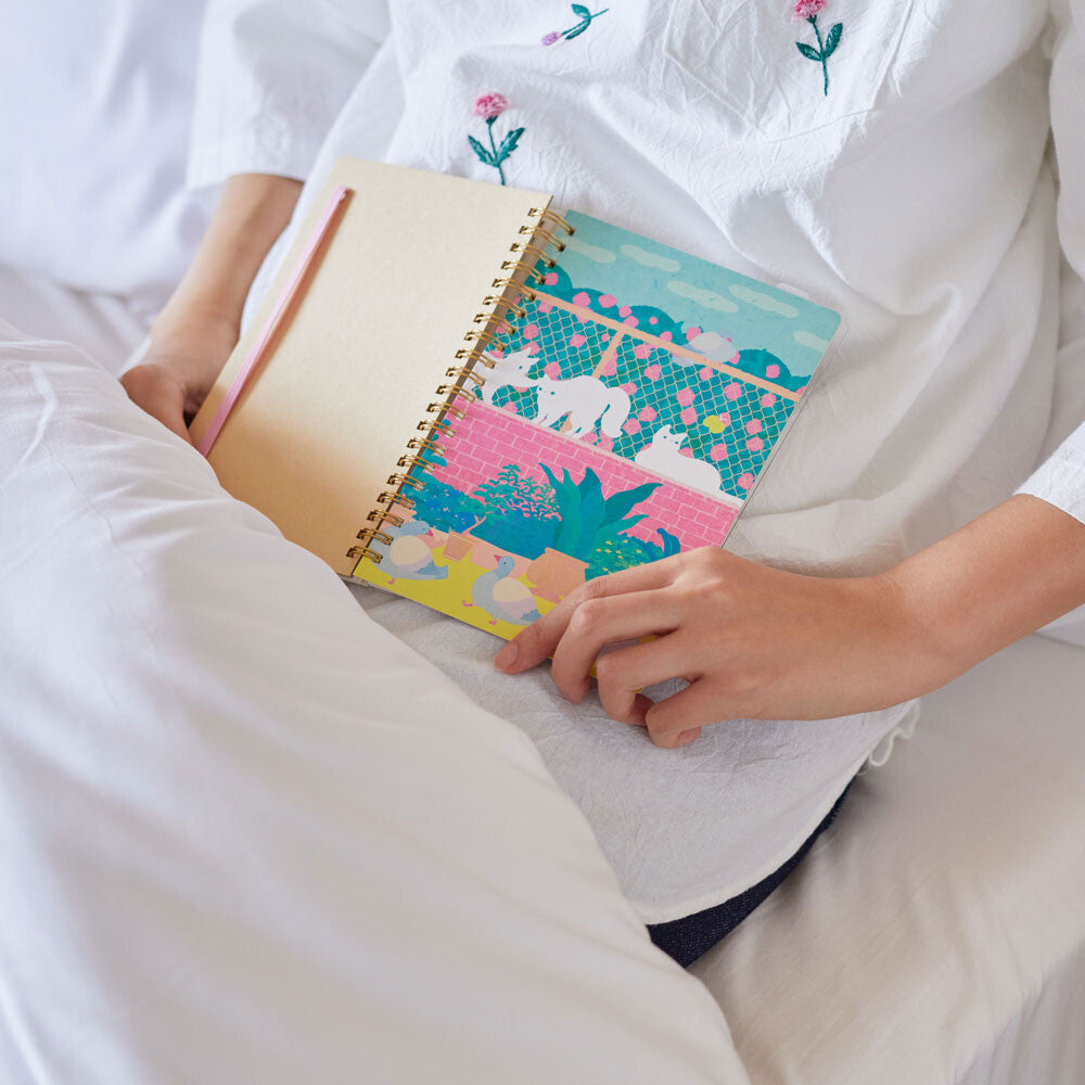 Comic-size ring-bound notebook featuring playful cats and garden illustrations by Zoomy BUNGU, with colorful cartoon cover design.