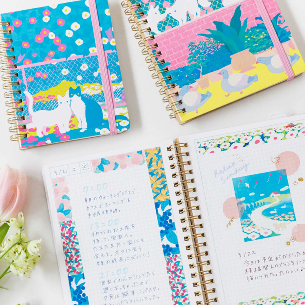Comic-size ring journal featuring playful cats and garden illustrations, by Zoomy BUNGU, shown with colorful cover and open pages.