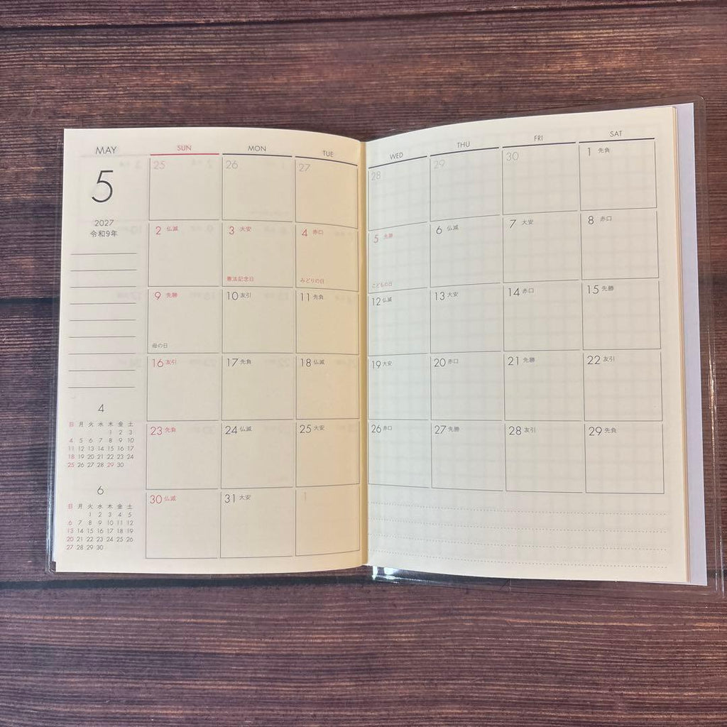 A6 monthly agenda planner in Wisteria by JapanoMono, featuring a soft purple cover and open pages for April 2026 to May 2027.